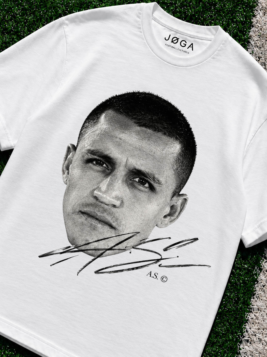 White JOGA oversized T-shirt with a black-and-white Alexis Sánchez face portrait, large signature graphic and A.S. © detailing printed on the front, photographed on green artificial turf zoomed in